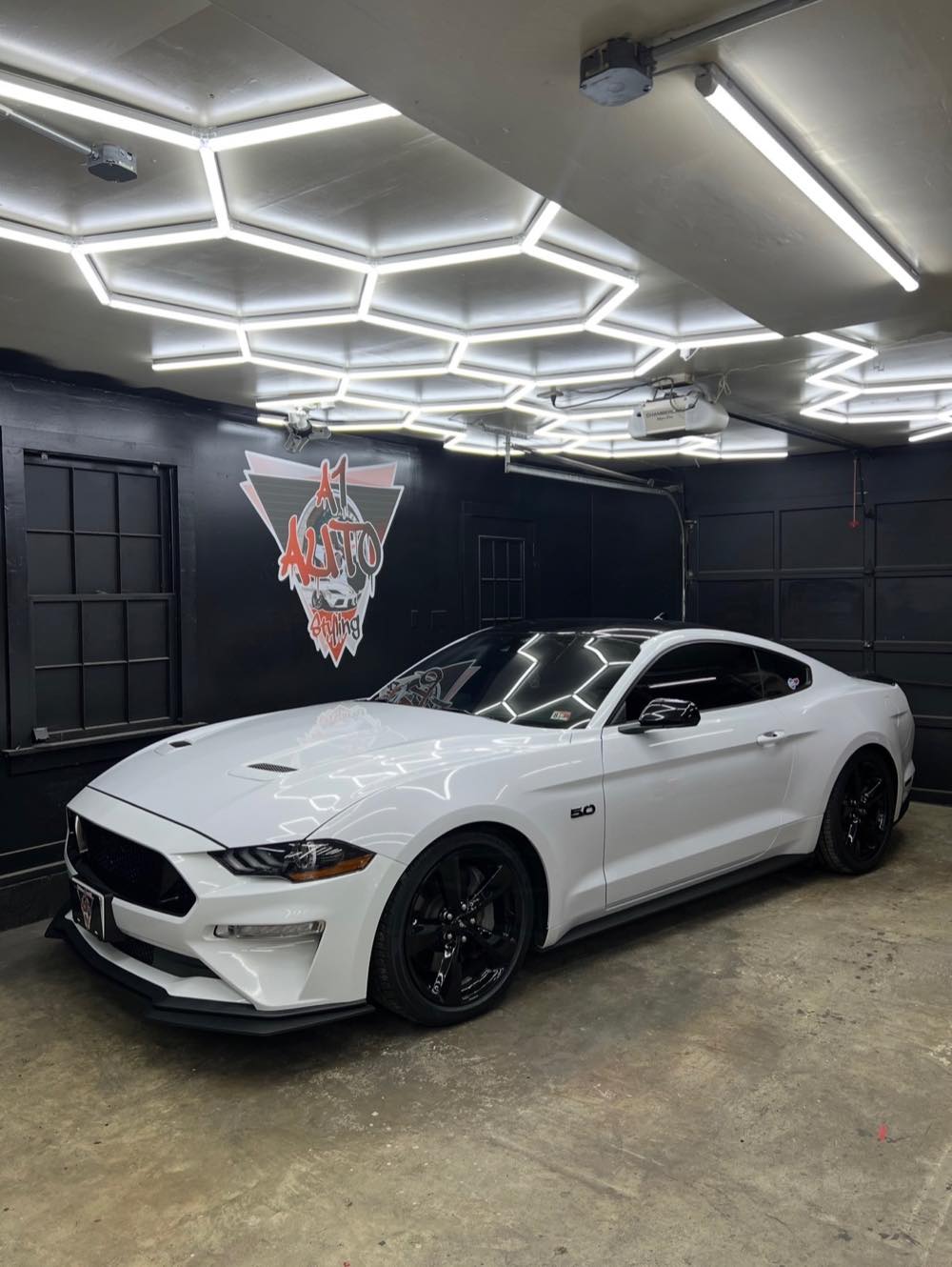 White Mustang GT inside the A1 Auto Styling bay in Manassas Park under hexagon lighting